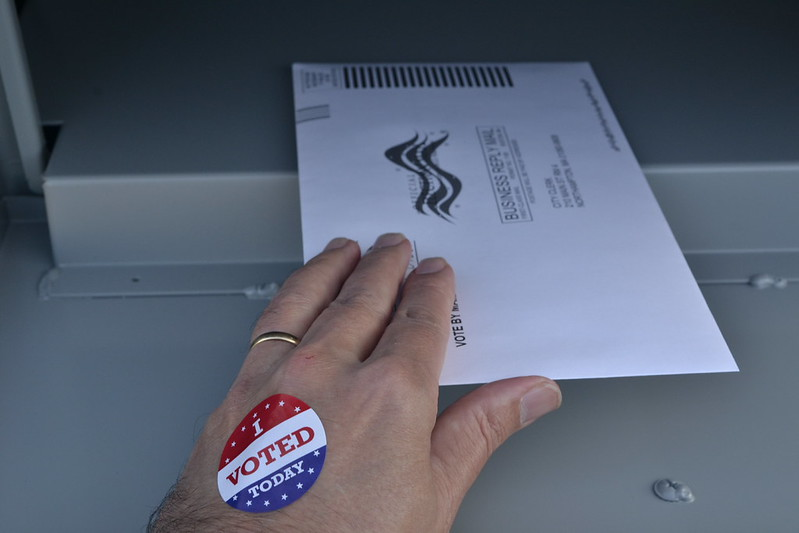 White hand putting mail-in-ballot through a slot.