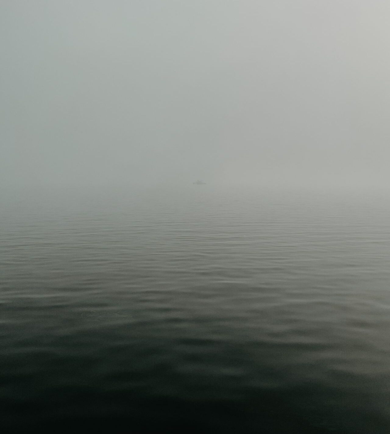 Fog over the ocean, with a small craft barely visible in the distance
