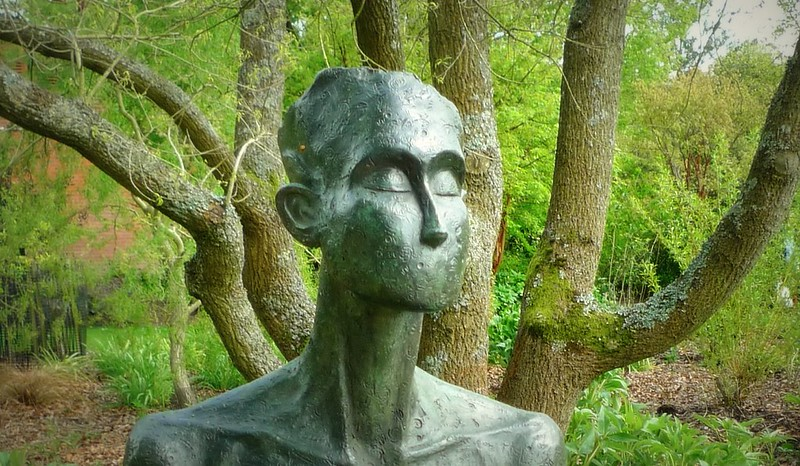 Set in front of a tree, a metal sculpture of person with no mouth
