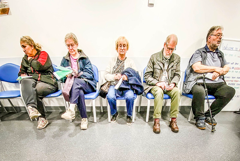 Five people sitting unhappily in a waiting room, avoiding each other.