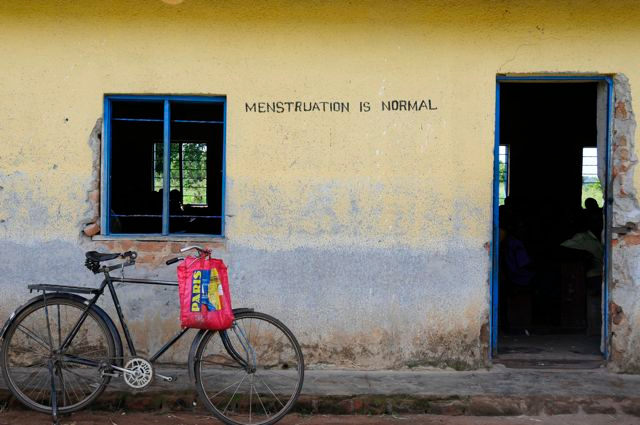 Photo of a bicycle leaed against an exterior that is painted with the message "Menstruation is normal."