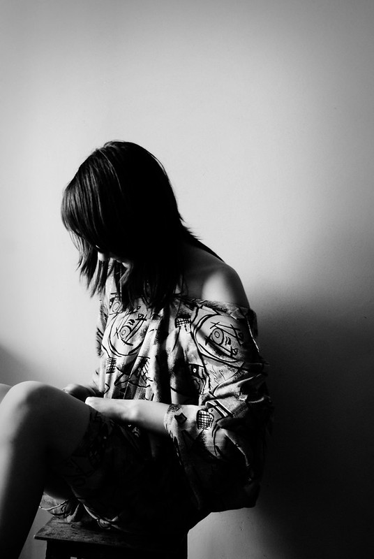 B&W photo of a female figure sitting in shadows, looking downward